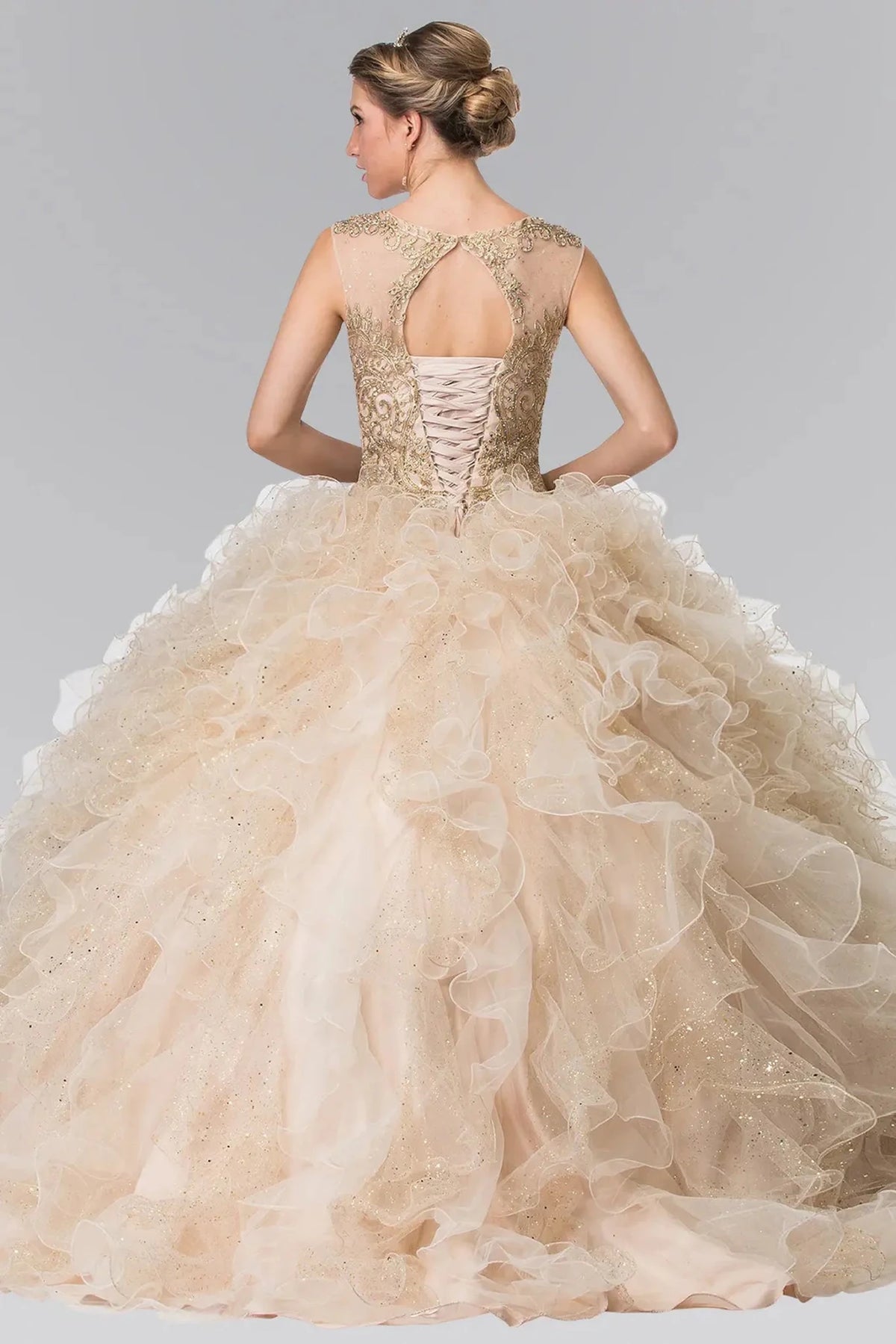 The Champagne quinceañera dress comes into focus in a full back view, showing a keyhole neckline and corset lacing above the ruffled skirt.