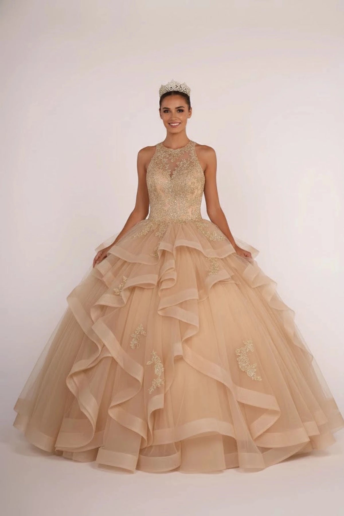 Full-length Champagne quinceañera ball gown showcases a gold halter bodice and champagne waterfall ruffles.
