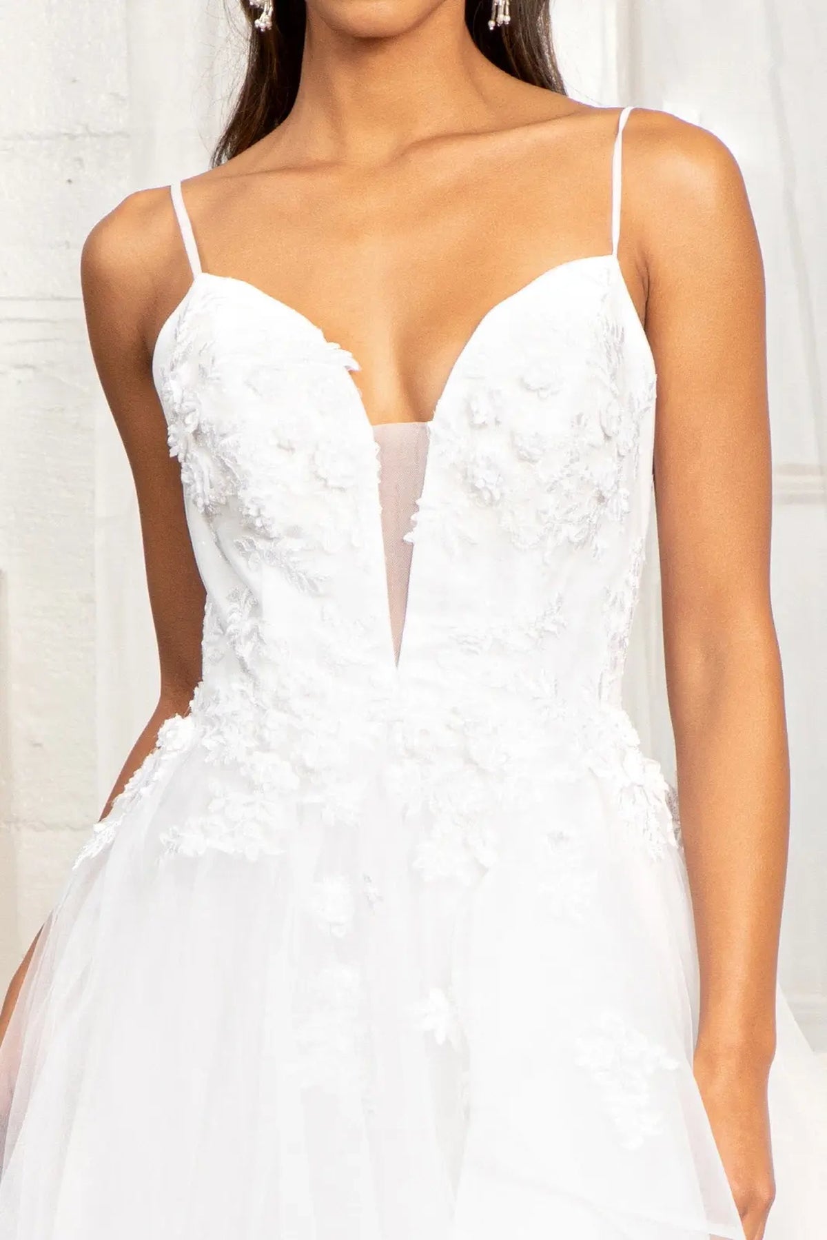 White wedding gown with raised blossoms edging its embroidered V-neck bodice.