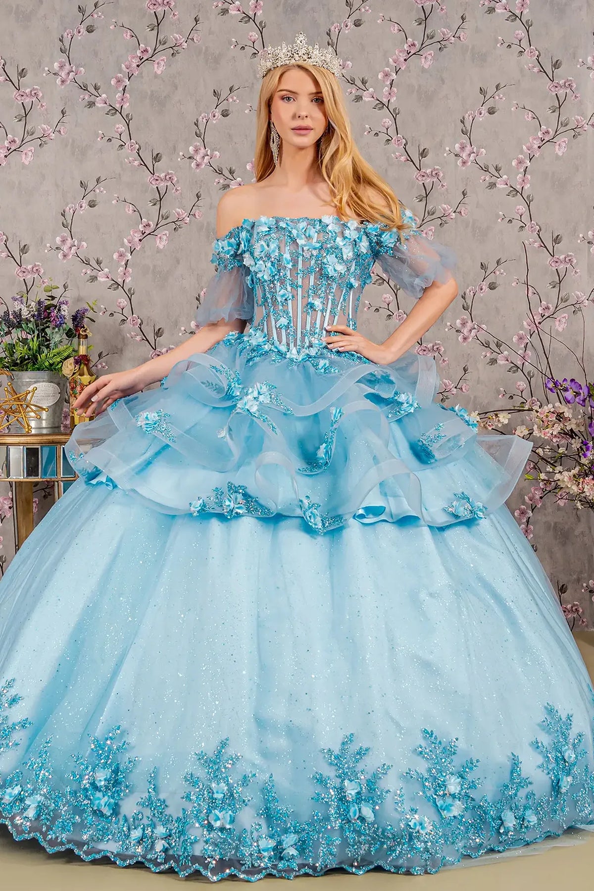 Embroidered details frame the Baby Blue quinceañera ball gown with ruffled skirt.