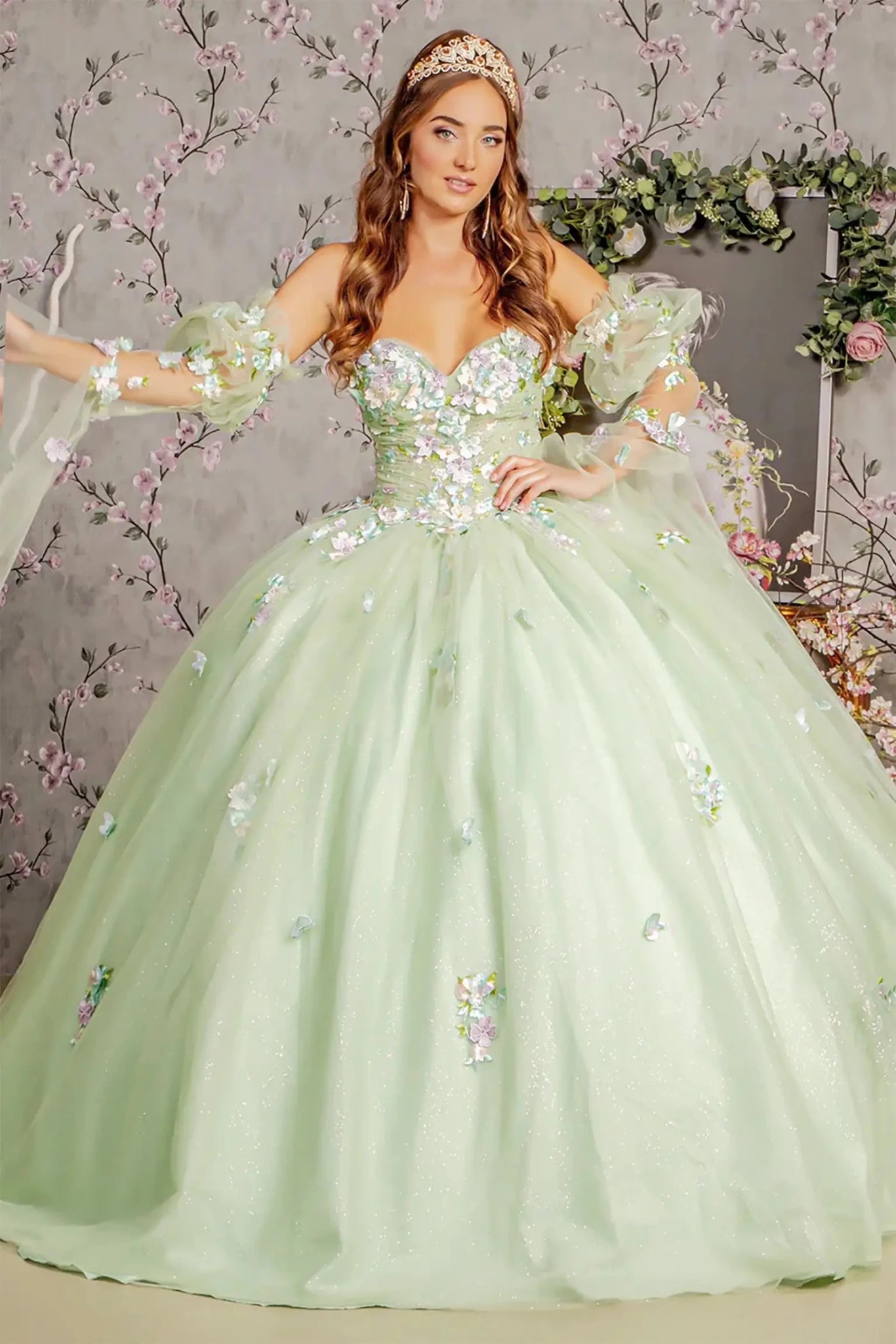 Woman in a light green sequined gown with floral embellishments against a decorative background.