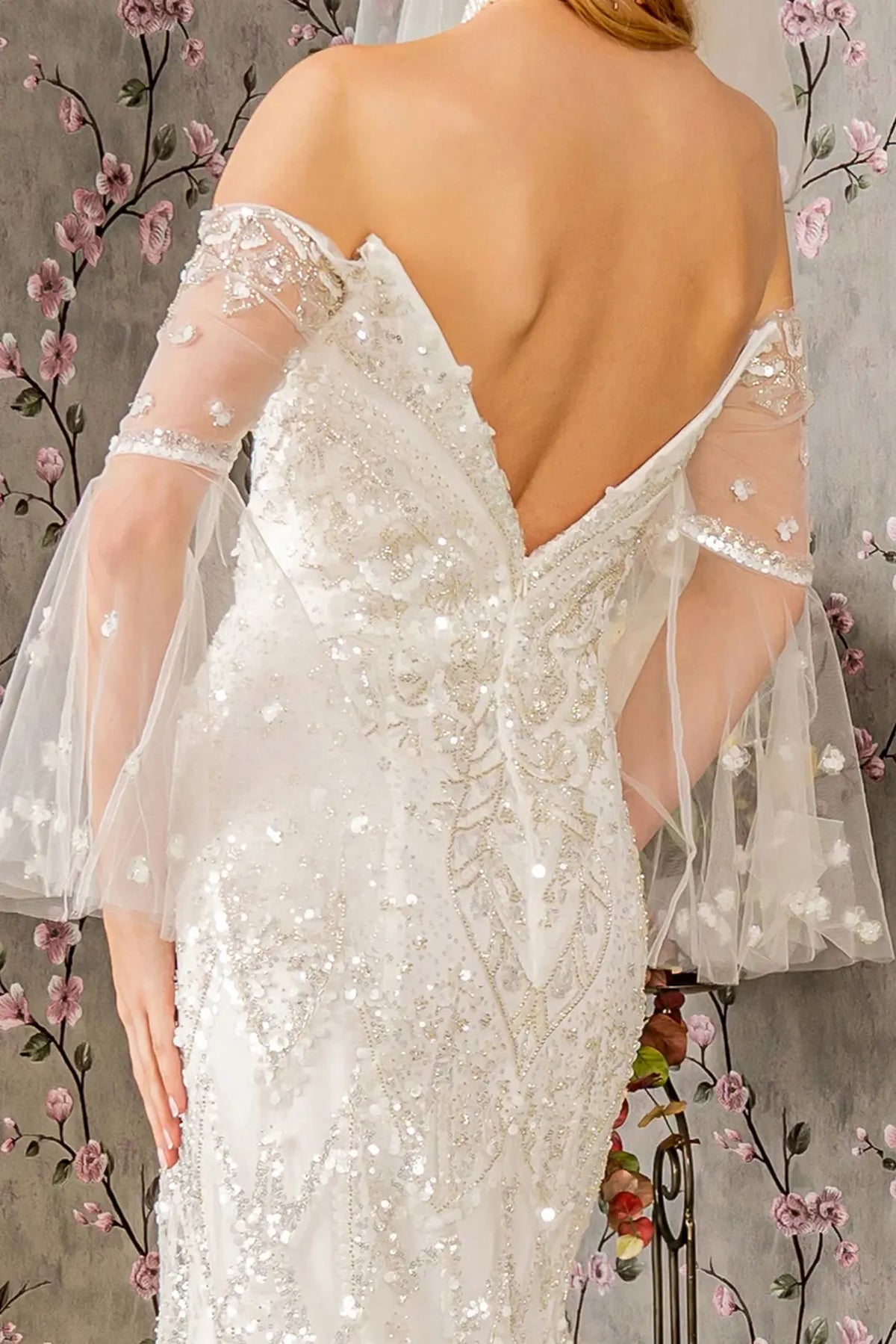 Sheer sleeves drape beside the beaded V-back of the ivory wedding gown.