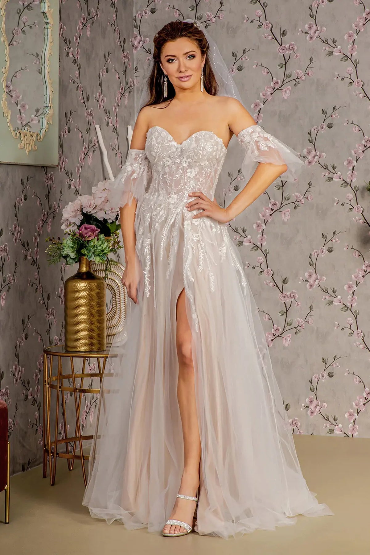 Detachable off-shoulder sleeves frame the Ivory/Champagne wedding gown above a softly layered skirt with a front slit.