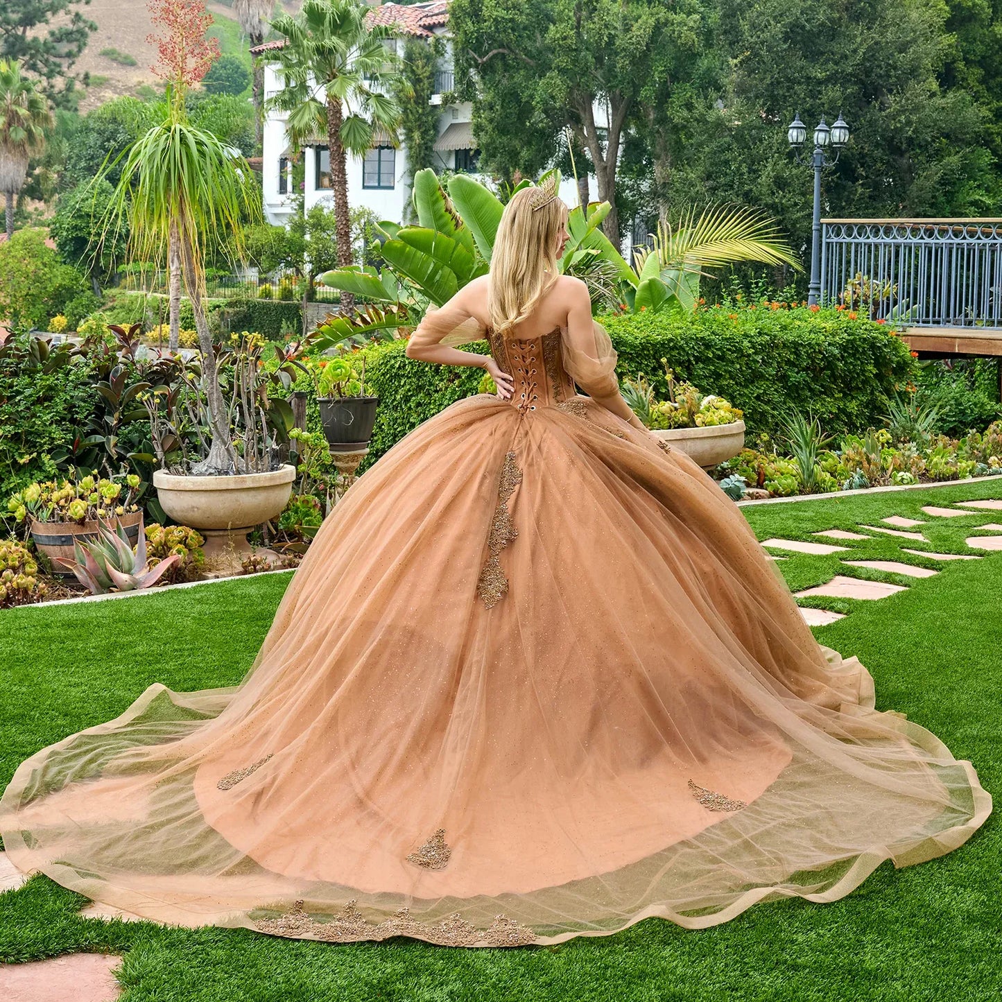 Woman in a peach-colored gown with a long train standing in a garden.