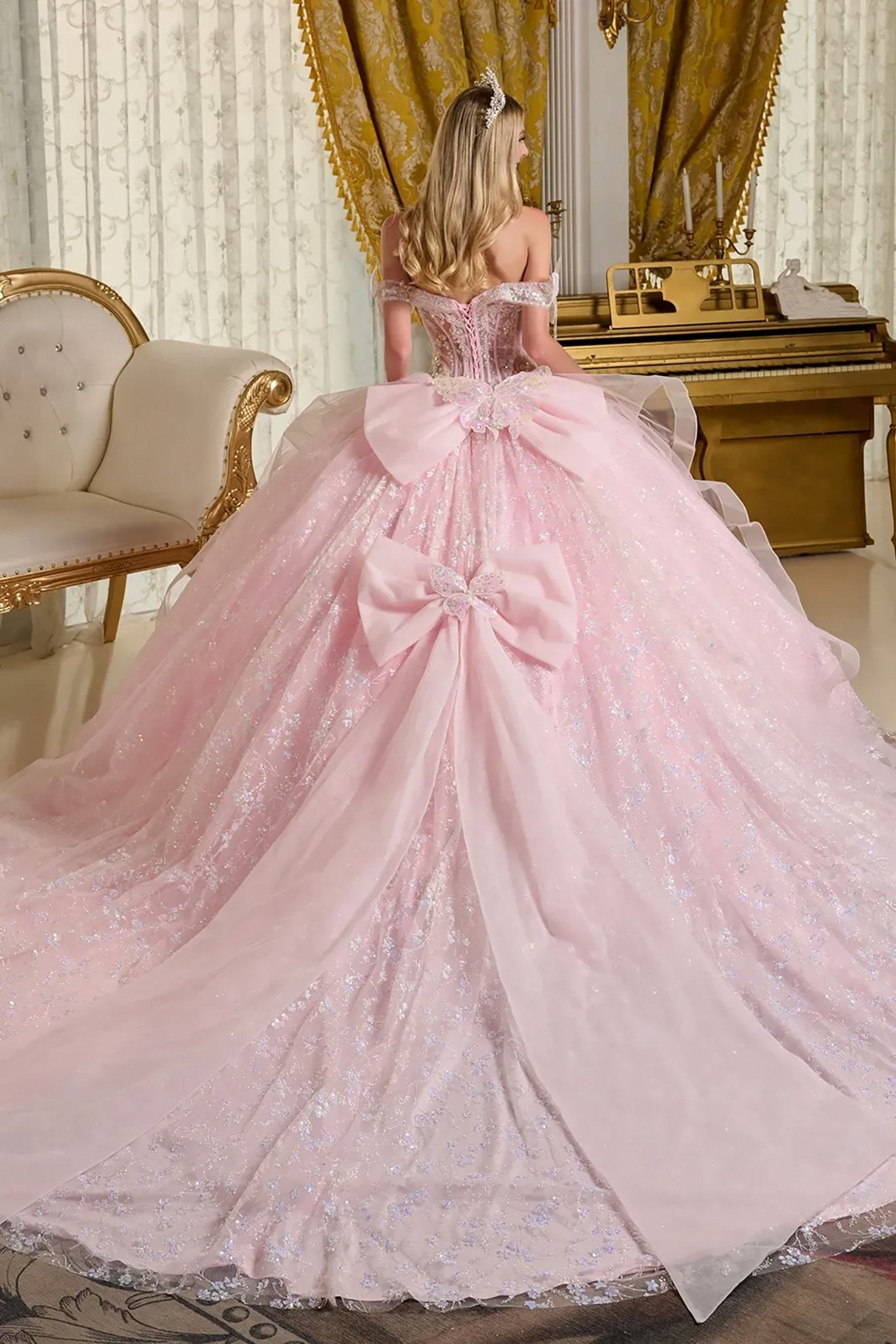 Woman in a pink ball gown with floral details with big ribbon in the back in an elegant room back view.