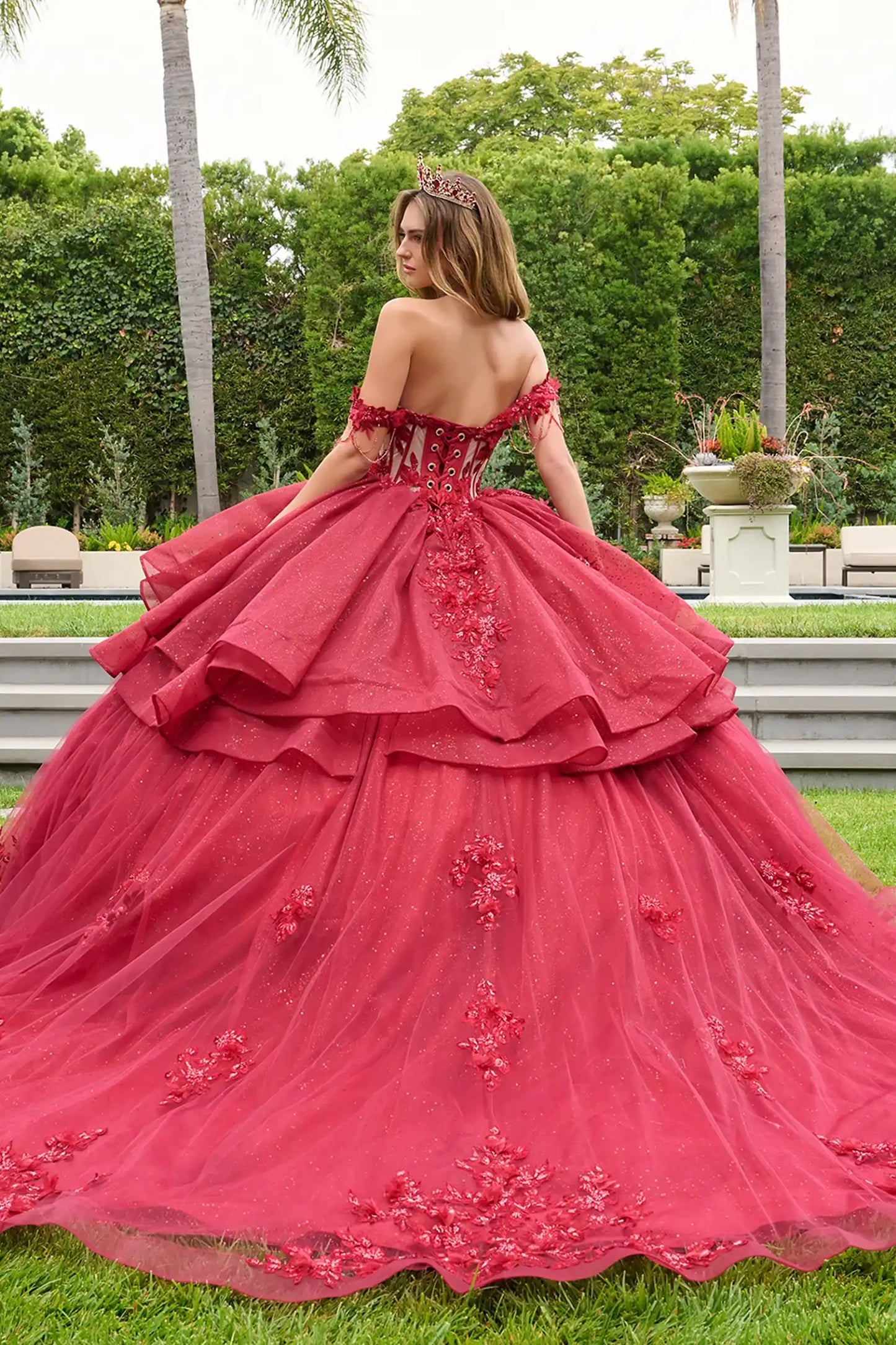 Red quinceañera ball gown showcasing lace-up bodice with bejeweled grommets and dramatic glitter overskirt train-length skirt
