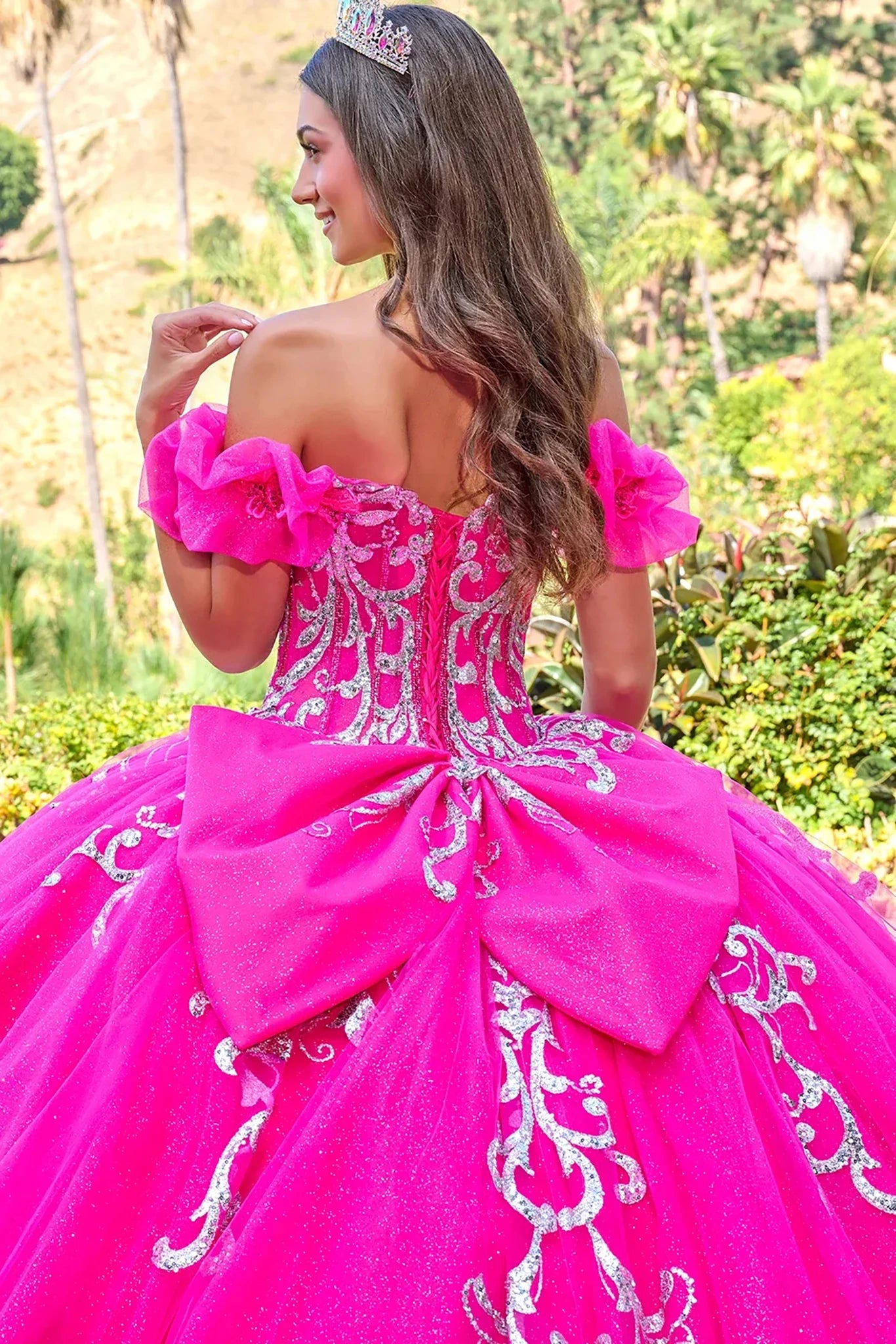 Woman in a fuchsia pink quinceañera dress with floral details outdoors.