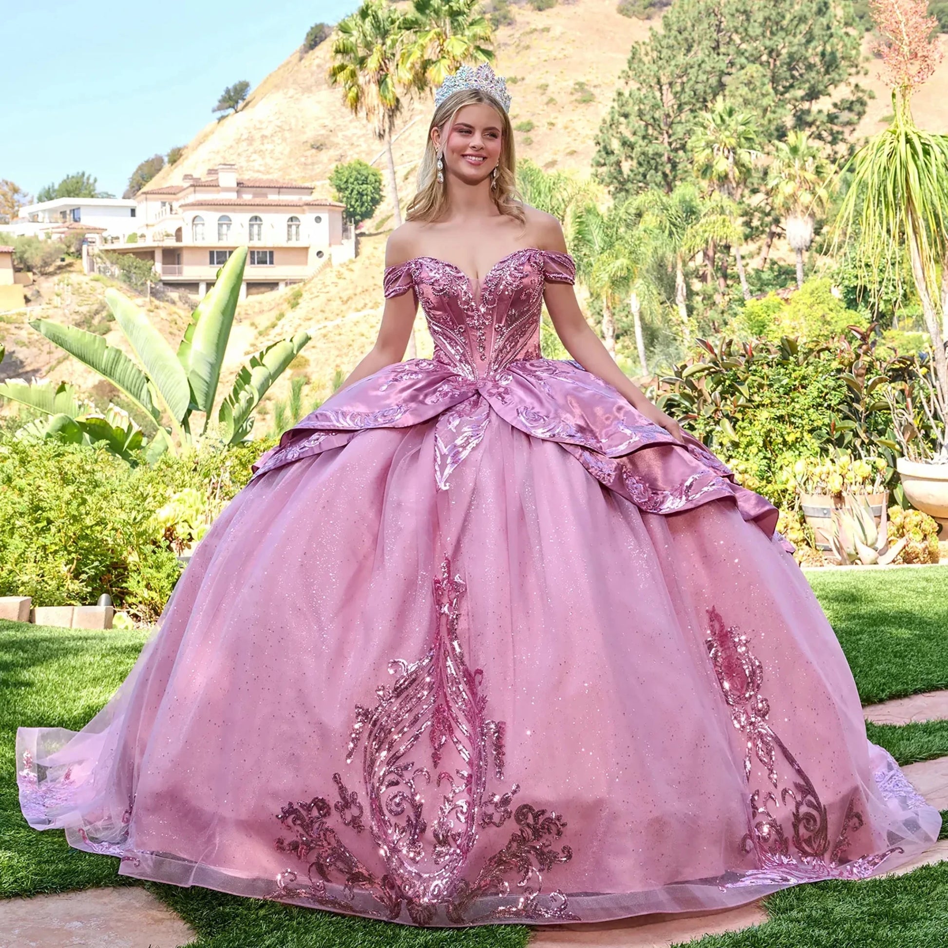 Woman in a dusty rose quinceañera dress standing outdoors with greenery and hills in the background