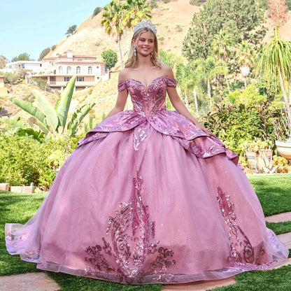 Woman in a dusty rose quinceañera dress standing outdoors with greenery and hills in the background