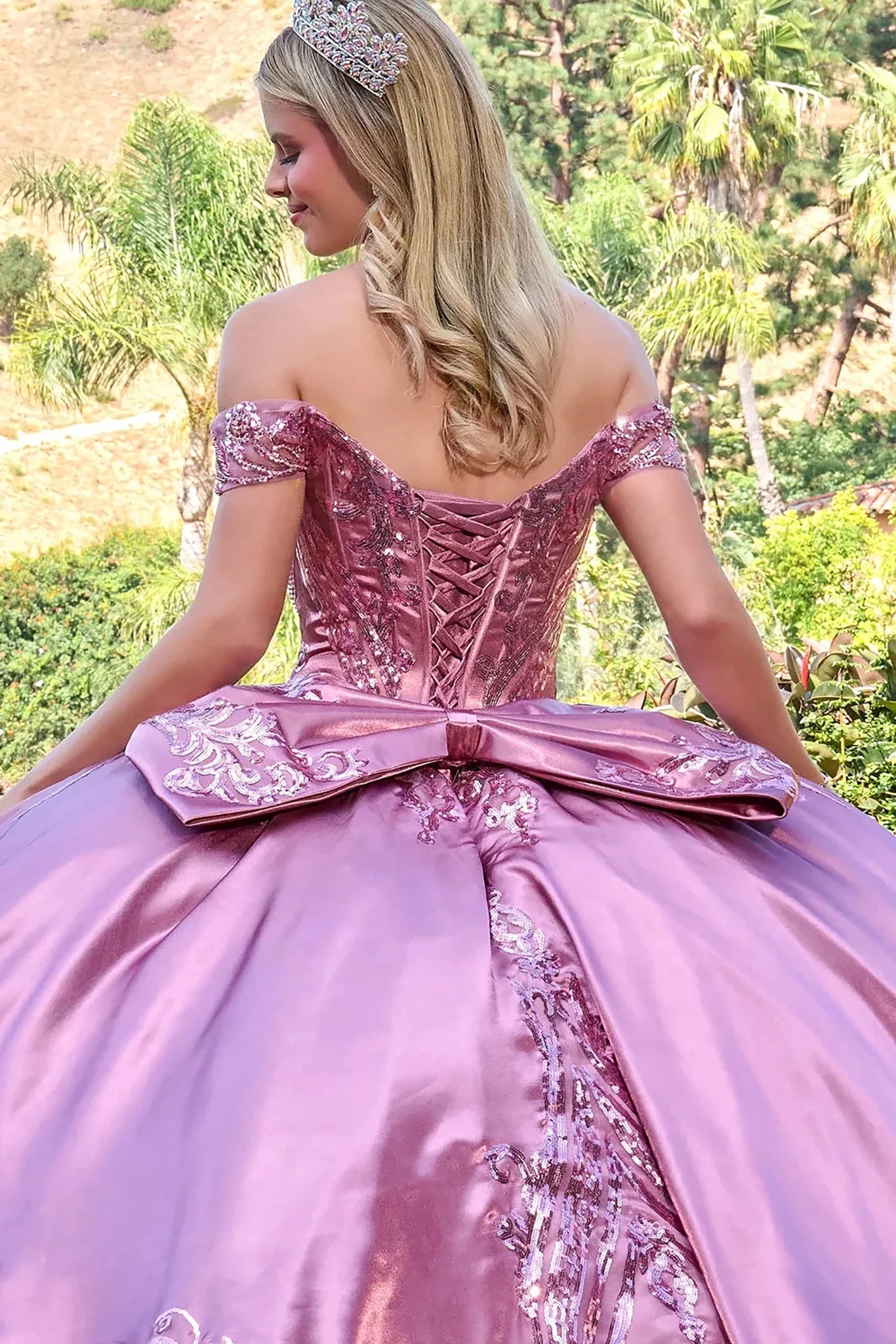 Woman in a dusty rose ball gown with a large bow in an outdoor setting