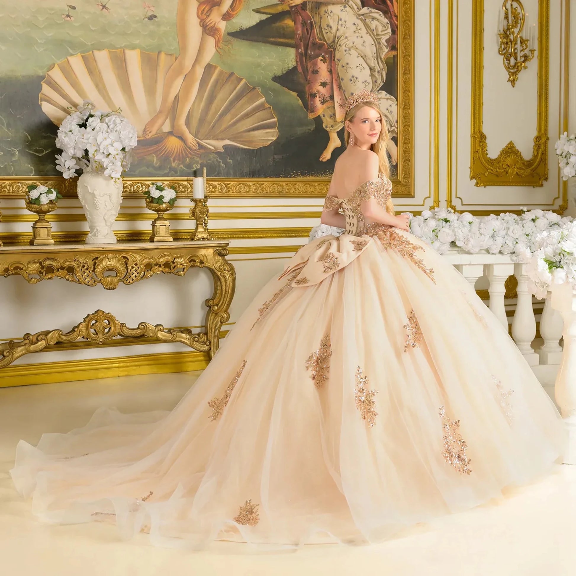Woman in a beige ball gown with floral details in an ornate room.