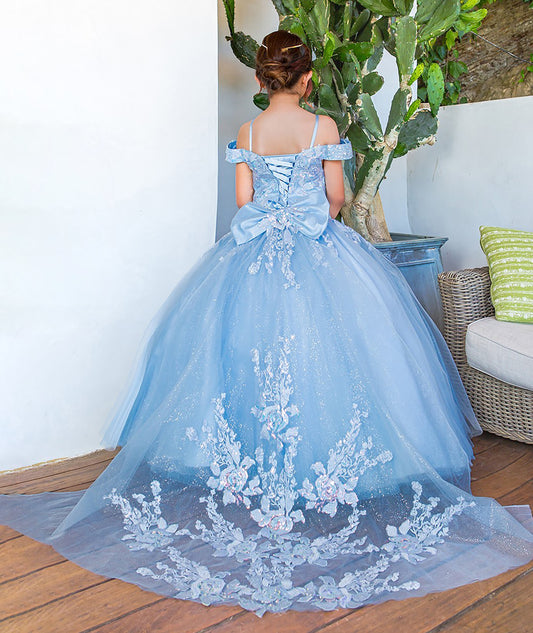 girl in a blue off-shoulder gown with floral embroidery standing in a room with a plant and chair.