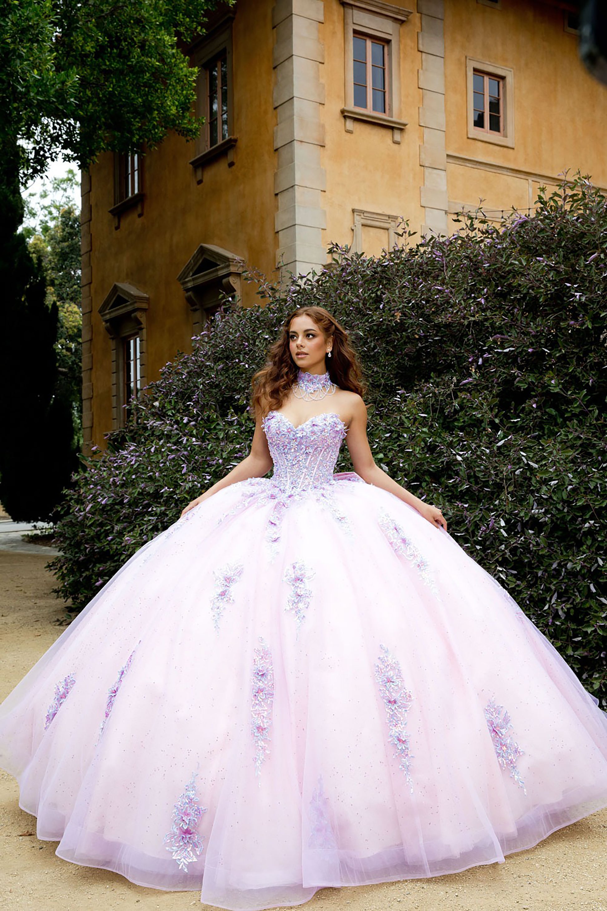 Woman in a purple floral dress standing in front of a building with greenery