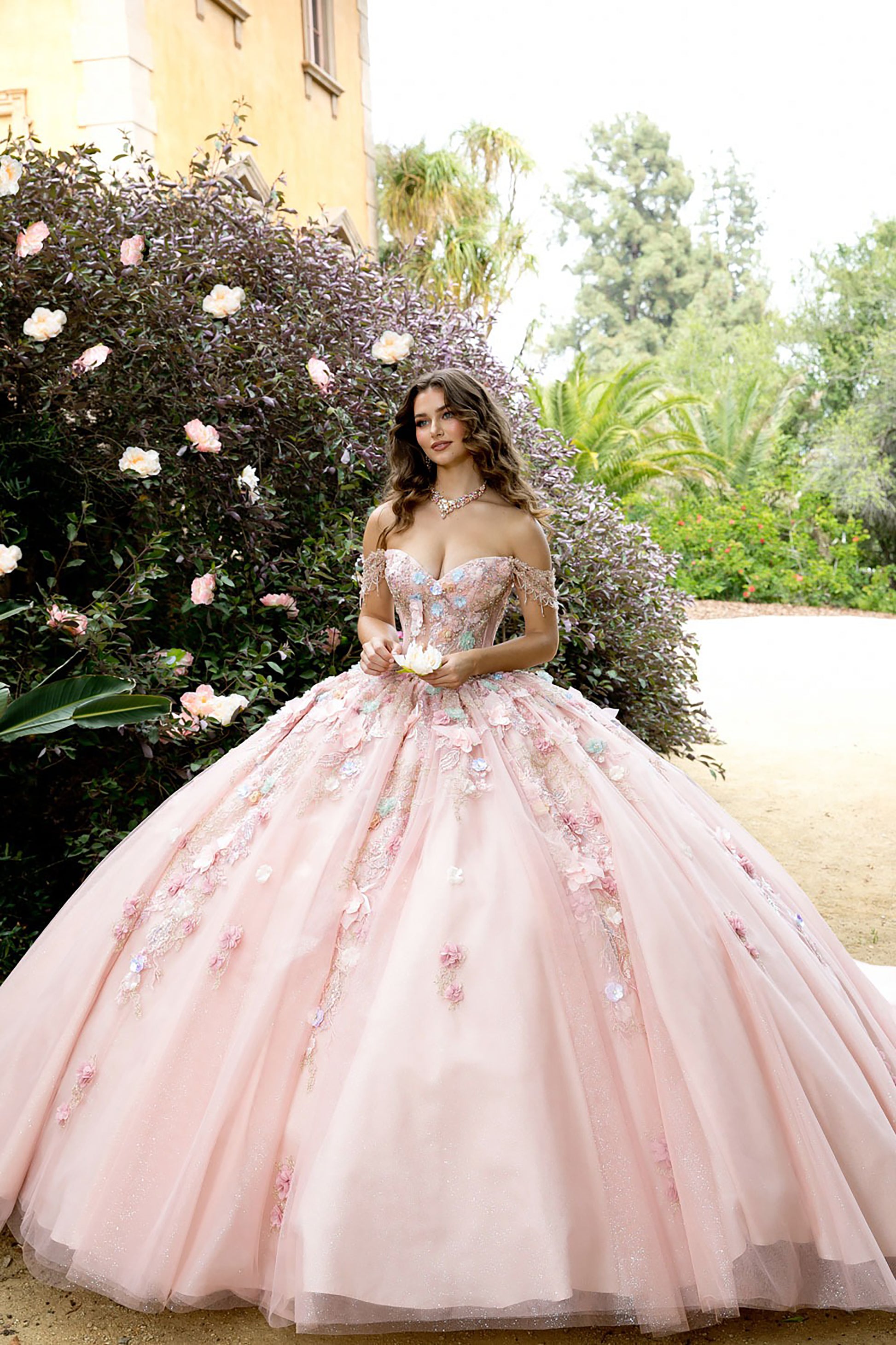 Woman in a pink floral dress standing in a garden with flowers and trees in the background