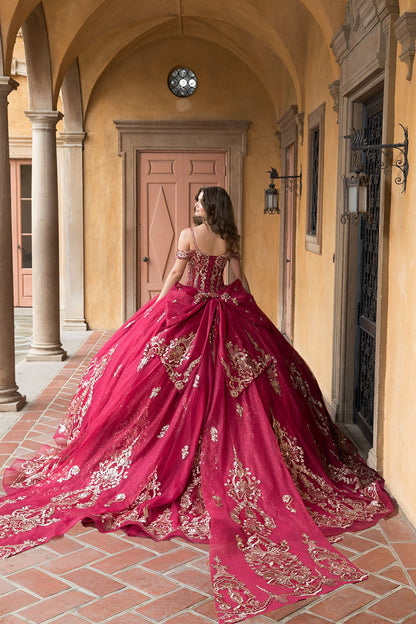 Woman in a red and gold embroidered gown standing in an outdoor setting with columns and a door.
