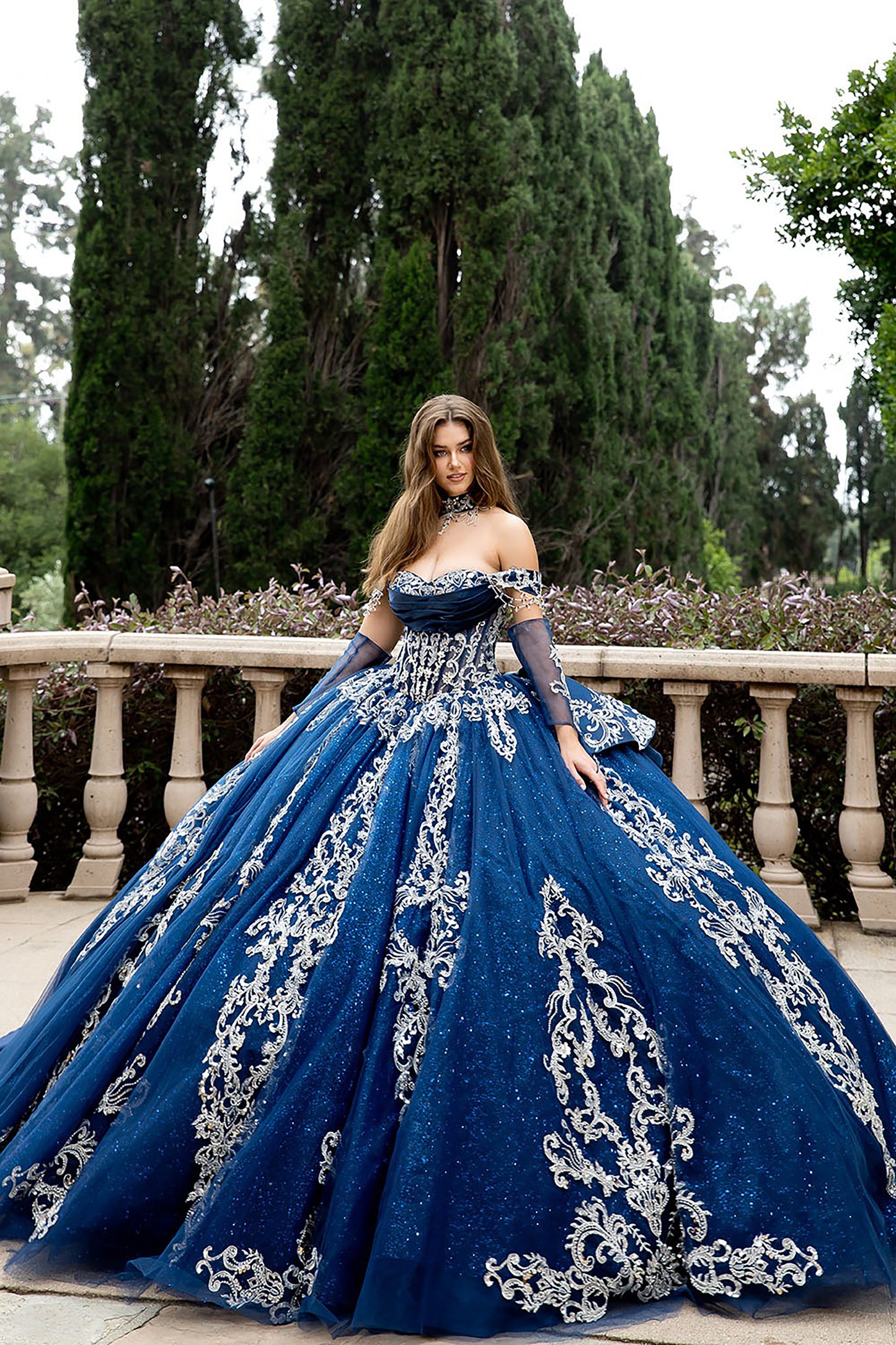 Woman in a blue evening gown with silver embroidery standing outdoors.