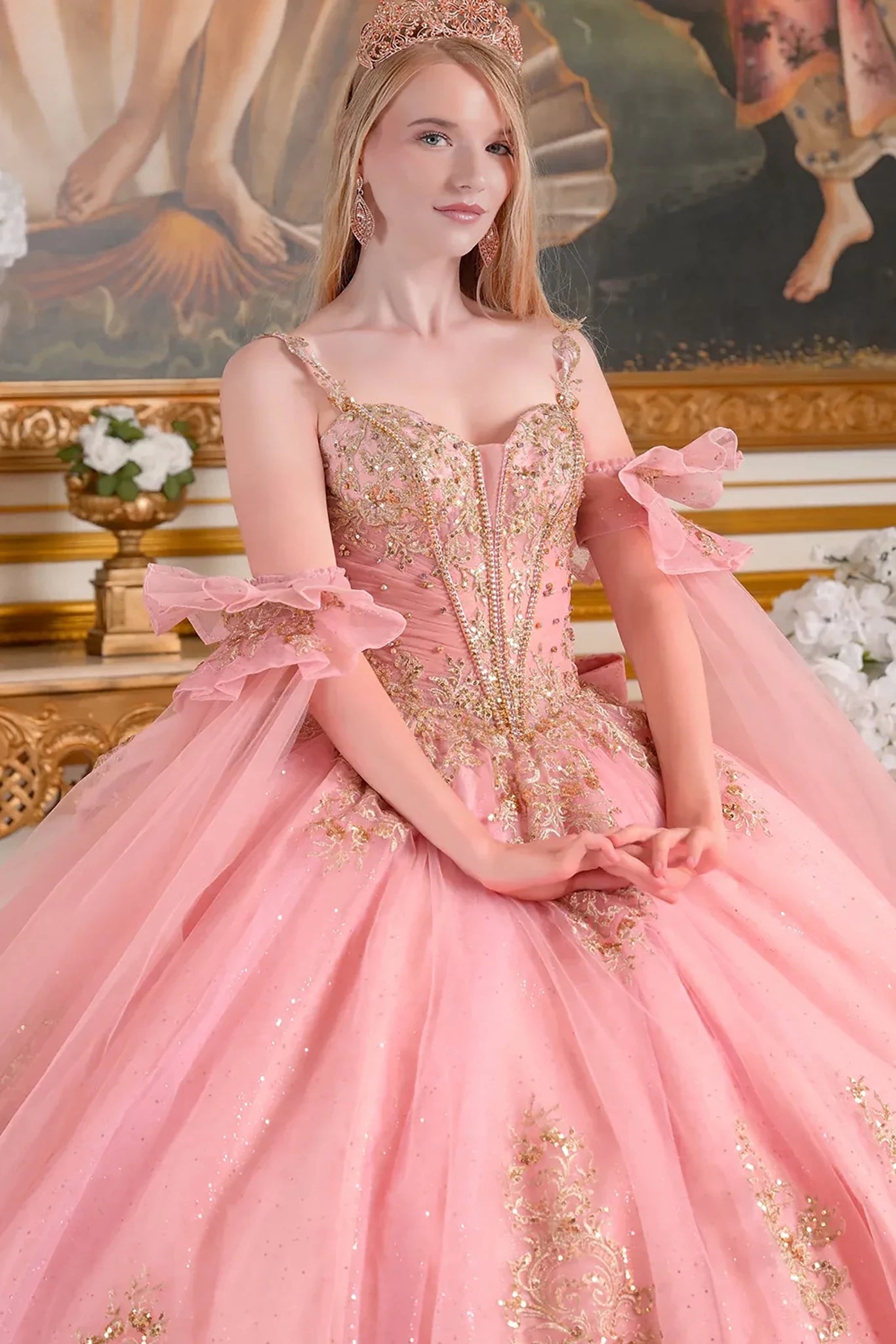 Woman in a dusty rose and gold dress with a tiara, sitting in an ornate room.