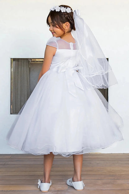 Young girl in a white dress showing her back with a veil standing indoors.