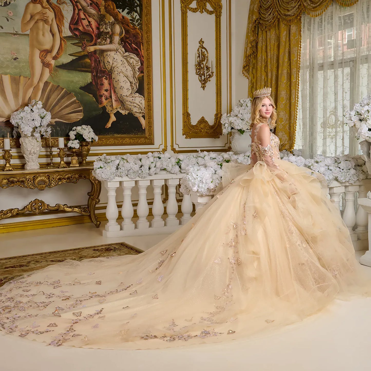 Woman in a beige gown with floral details in an opulent room with gold accents and classical painting.