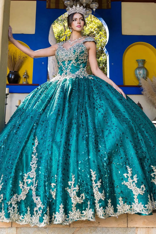 Woman in a hunter green ball gown with light gold embroidery standing in front of a decorative wall.