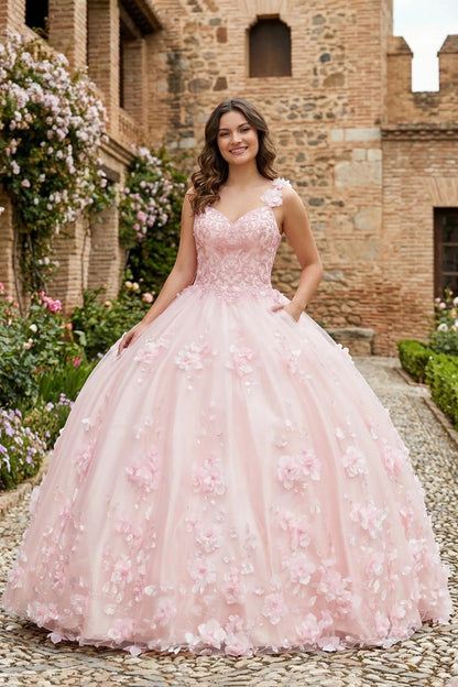 Girl in a pink floral quinceanera ball gown dress standing in front of a brick building with flowers.