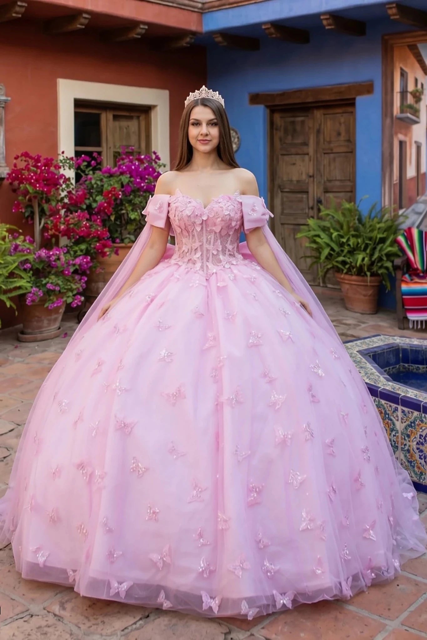 Woman in a pink ball gown with 3D butterflies standing in a colorful outdoor setting with flowers and a pool.
