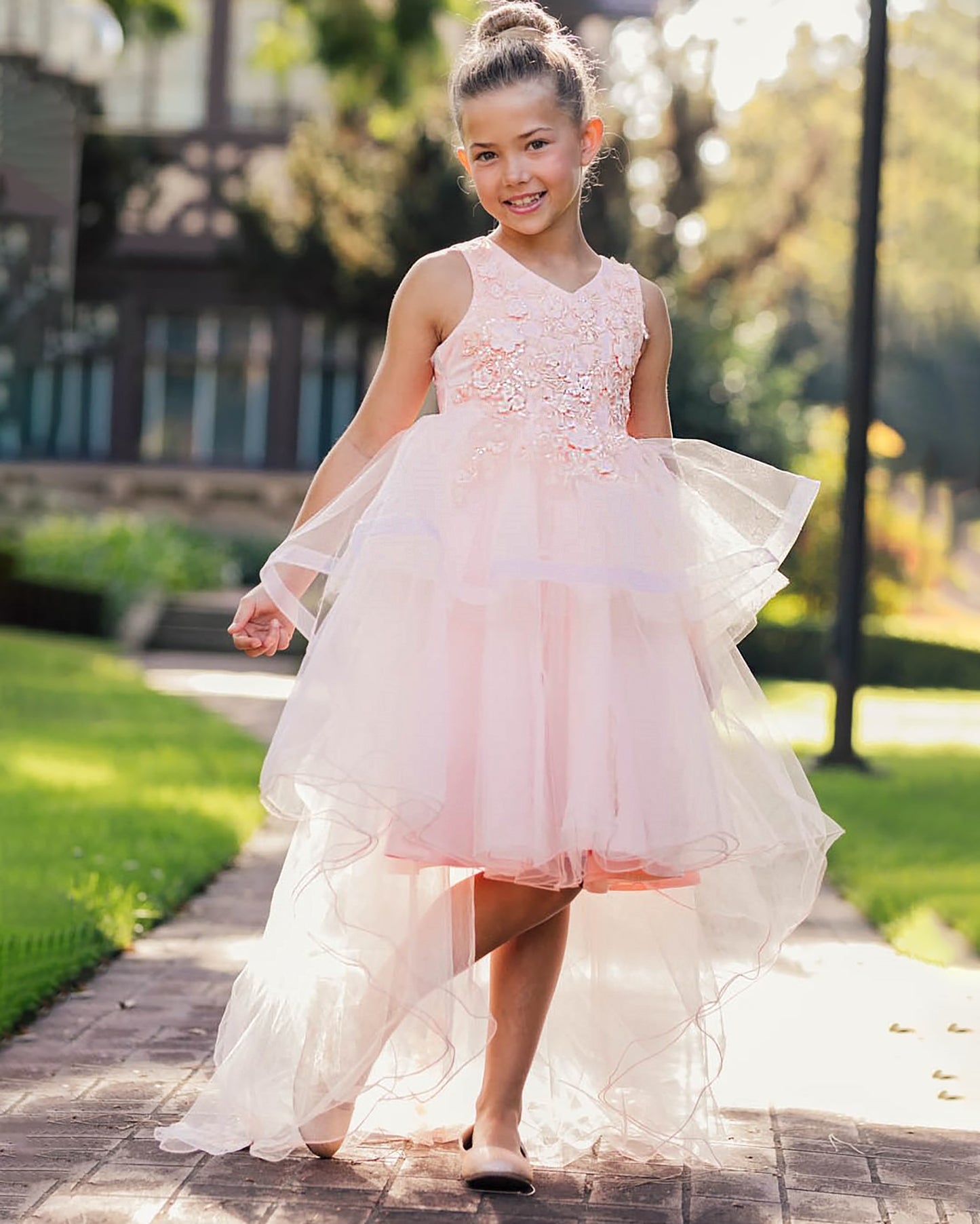 Young girl in a peach blush floral dress standing outdoors on a sunny day.