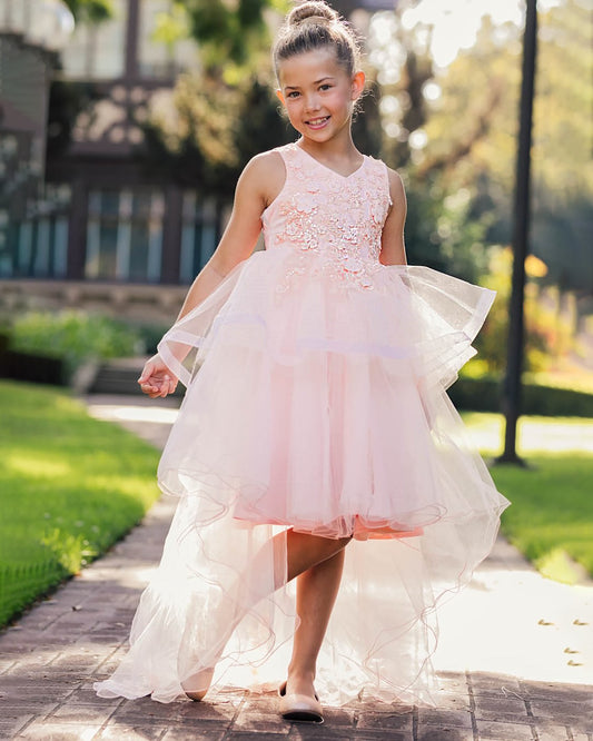 Young girl in a peach blush floral dress standing outdoors on a sunny day.