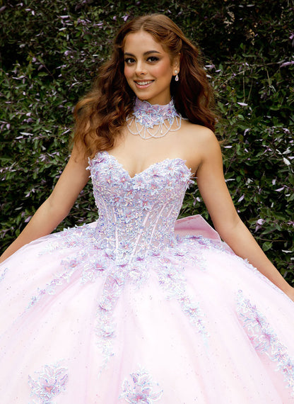 Woman in a pink and purple floral dress with a choker, sitting against a green leafy background.