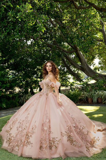 Woman in a pink and gold embroidered gown standing in a garden with trees and plants.