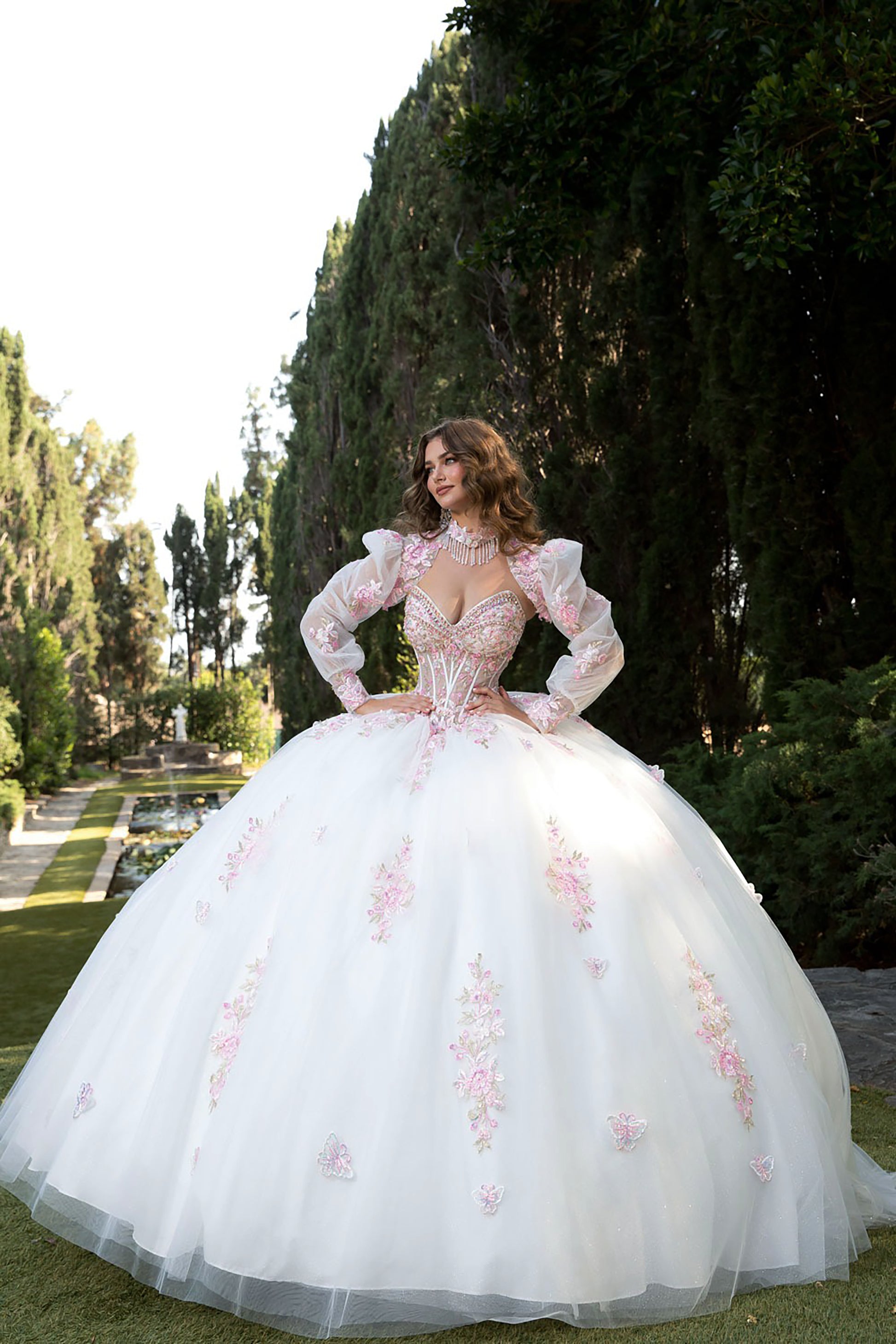 Woman in a white ballgown with floral details standing in a garden.