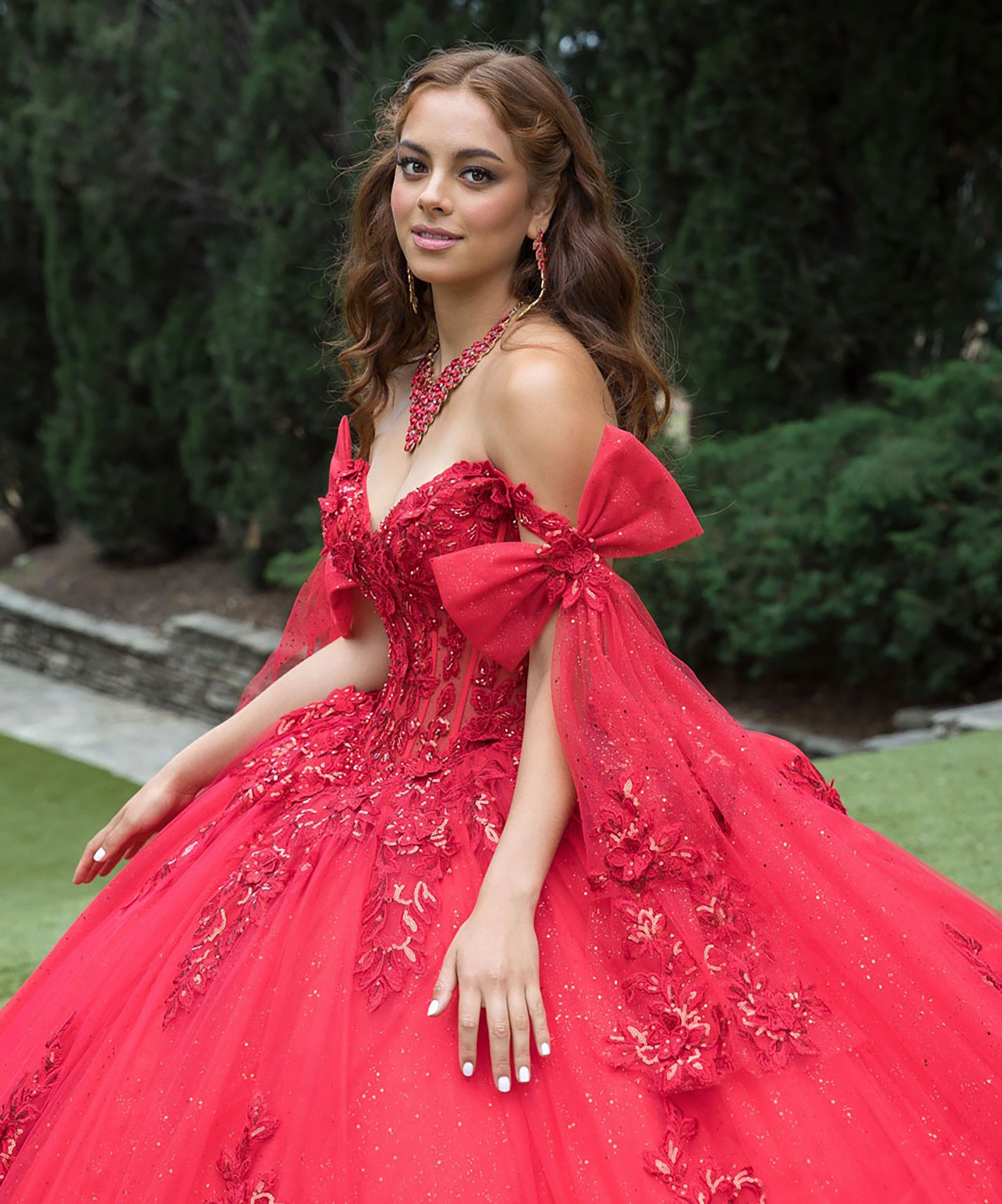 Woman in a red formal gown with floral details outdoors.
