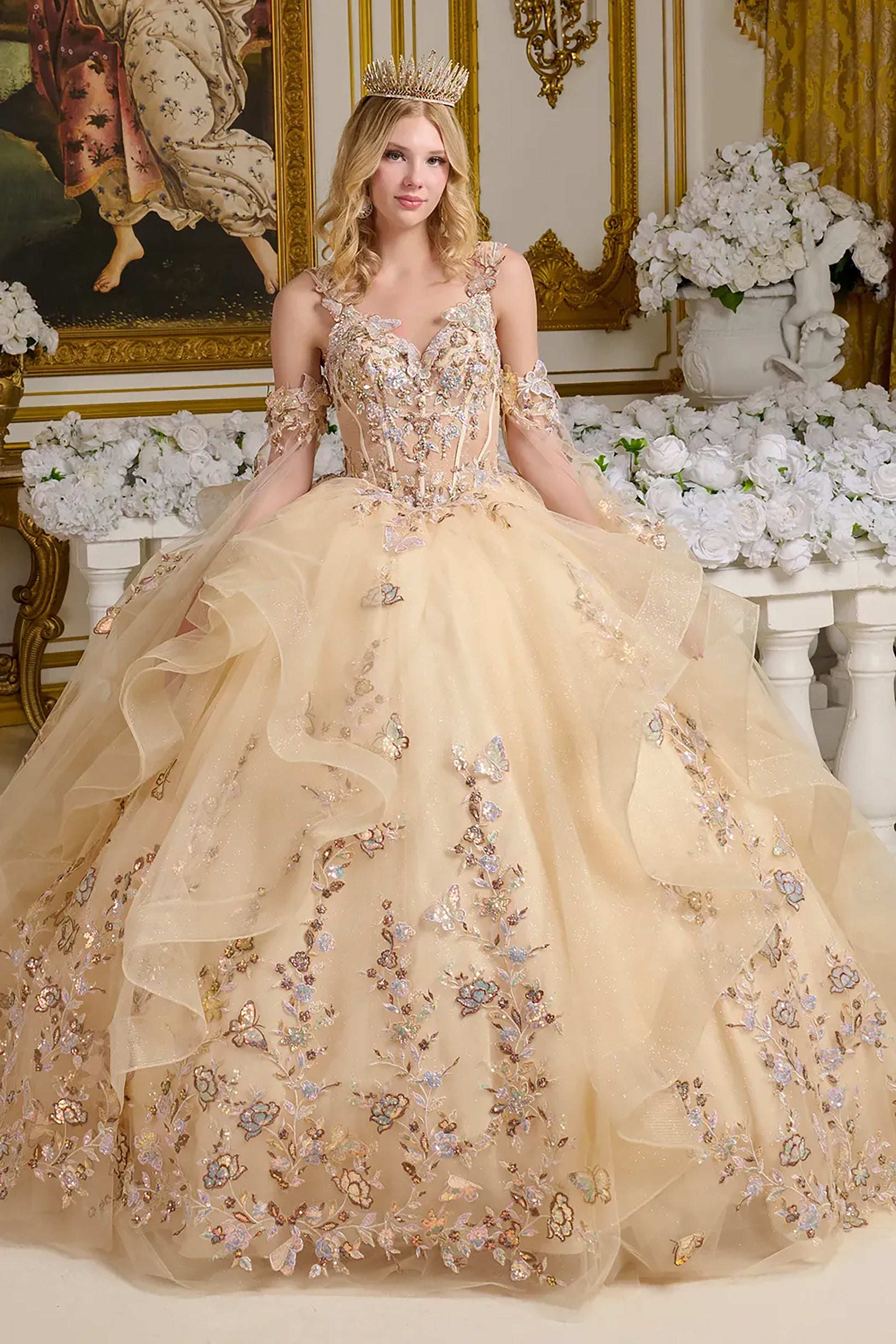Woman in a beige embroidered gown with floral details in an ornate room.