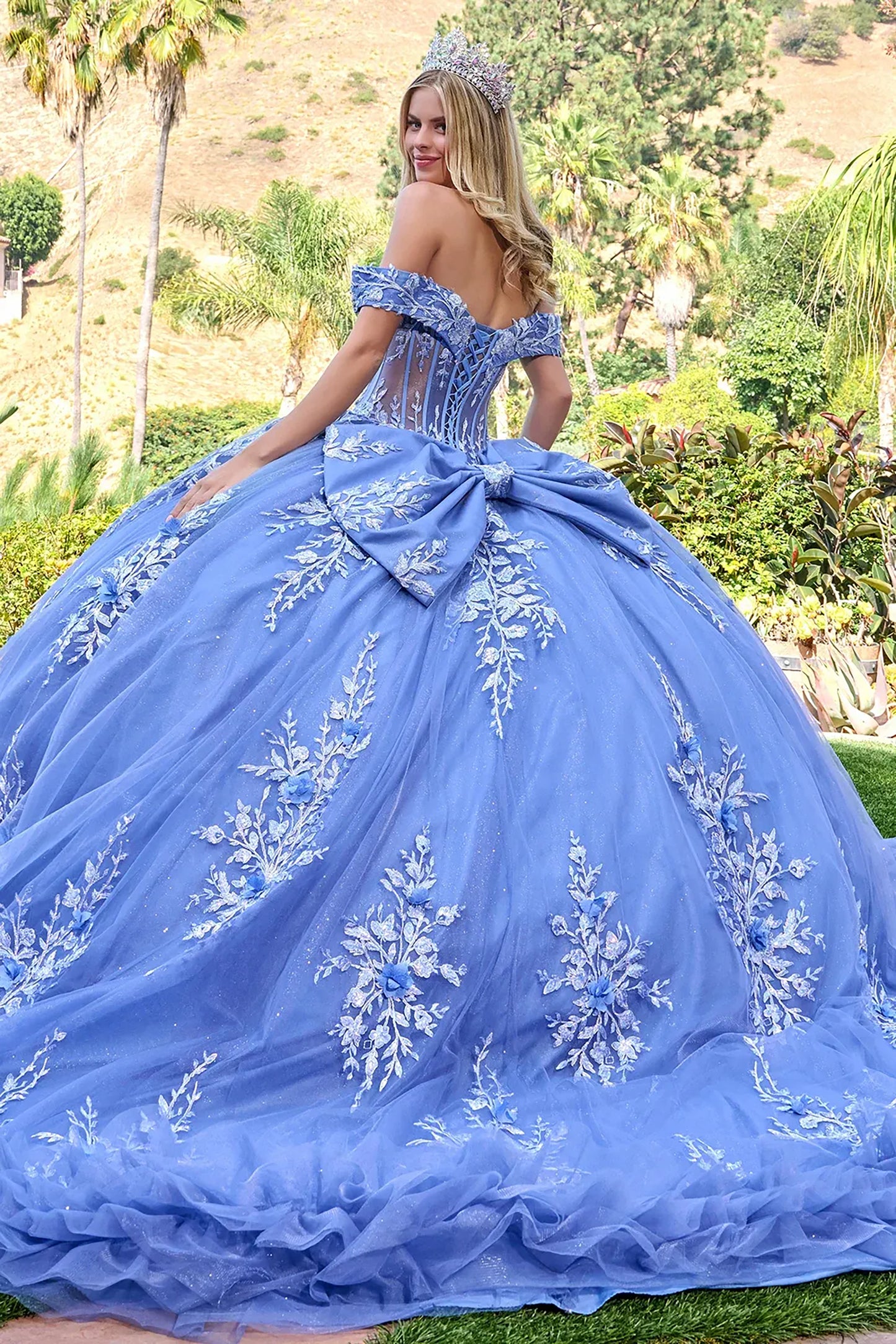 Woman in a dusty blue quince ball gown with floral embroidery in an outdoor setting.
