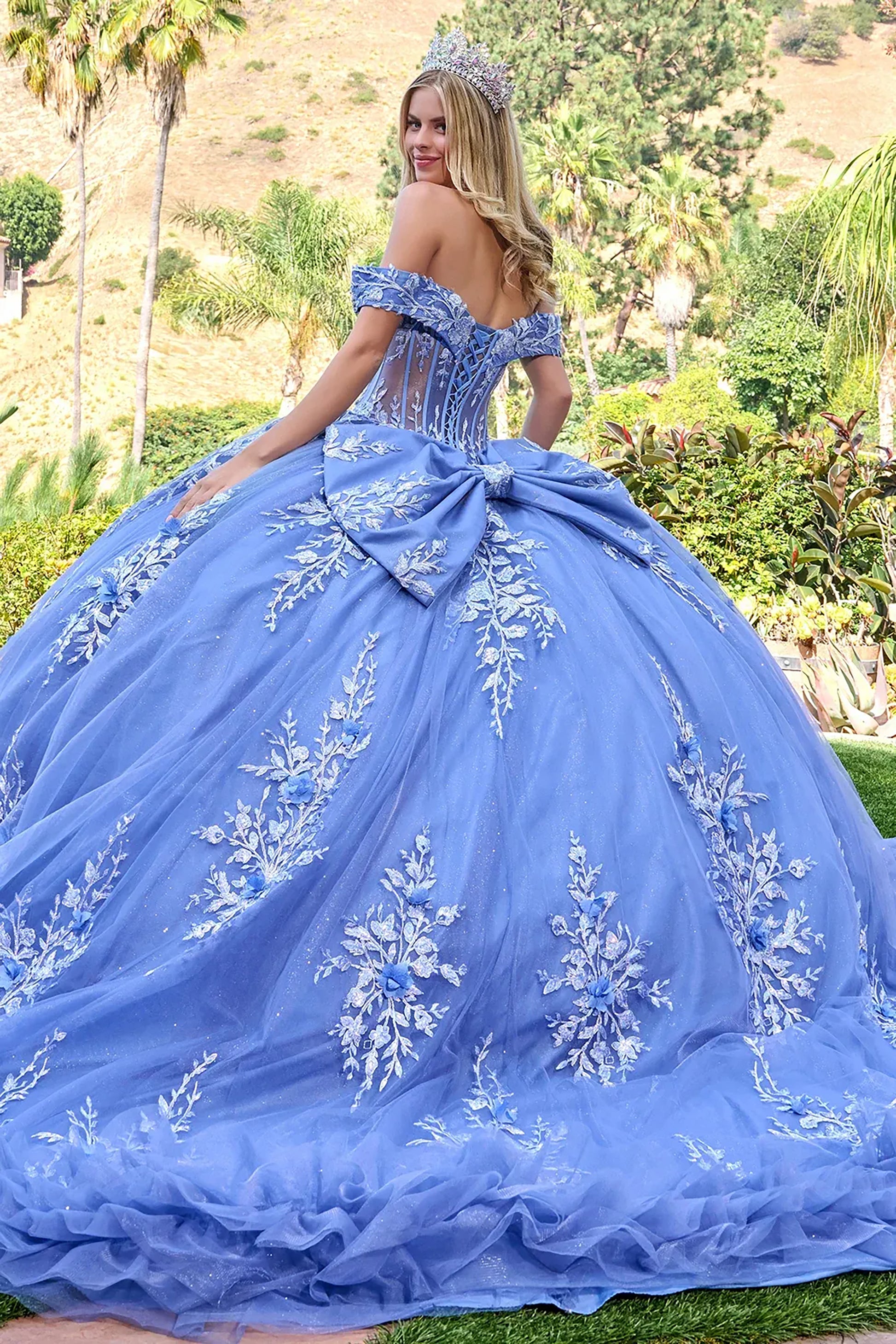 Woman in a dusty blue quince ball gown with floral embroidery in an outdoor setting.