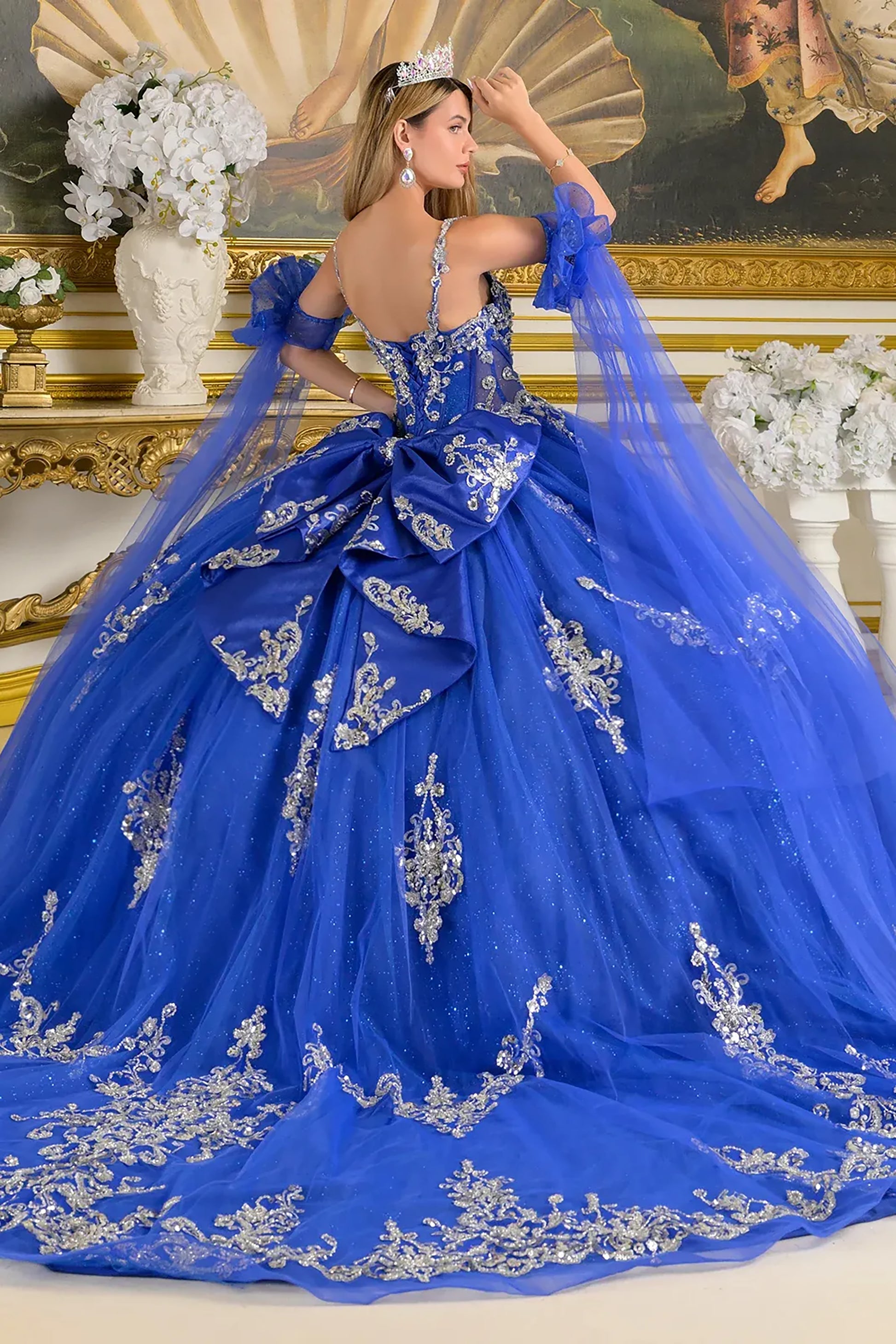 Blue ball gown with intricate silver embroidery in a decorated room.