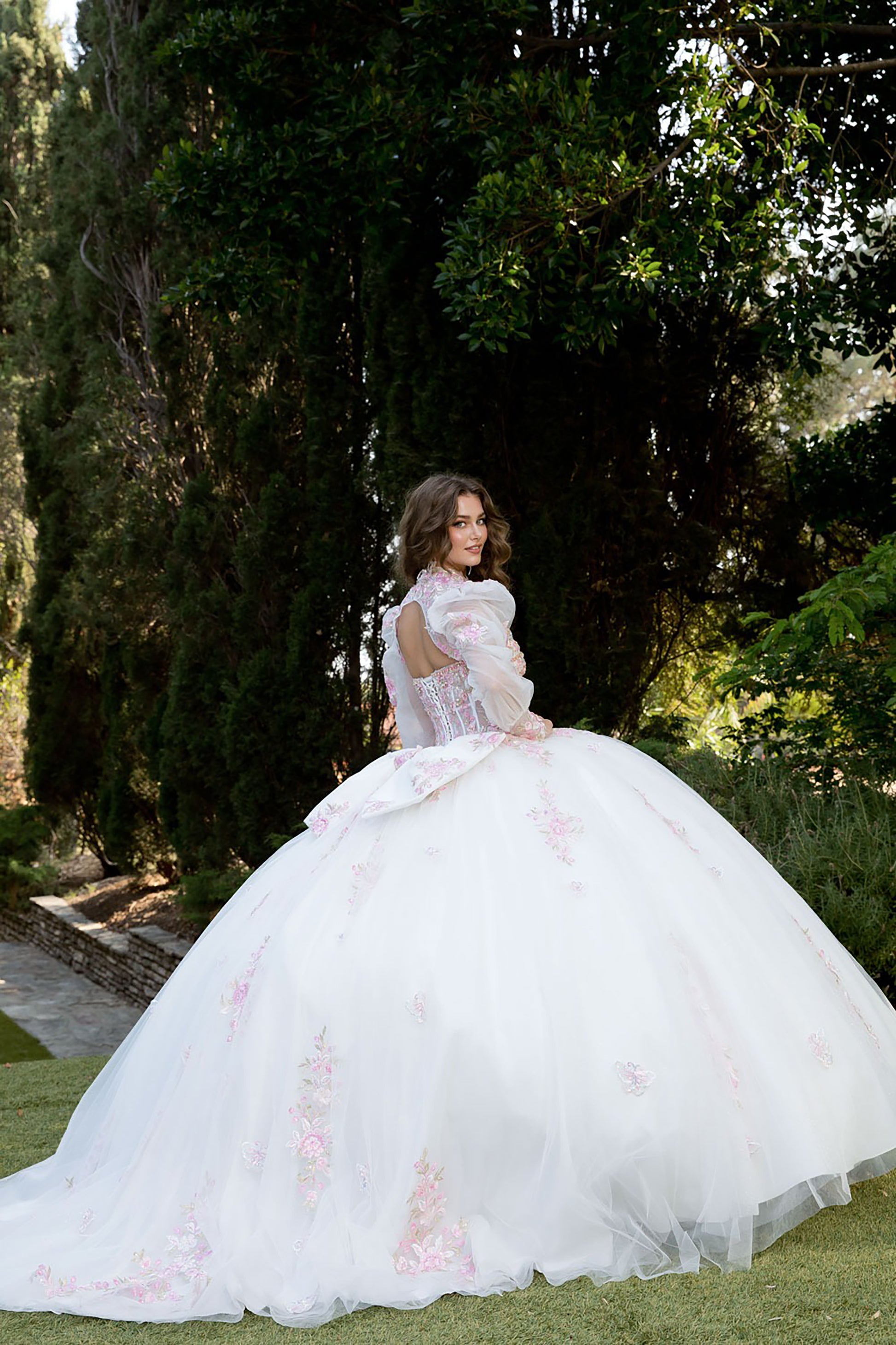Woman in a white ballgown with floral details standing in a garden.