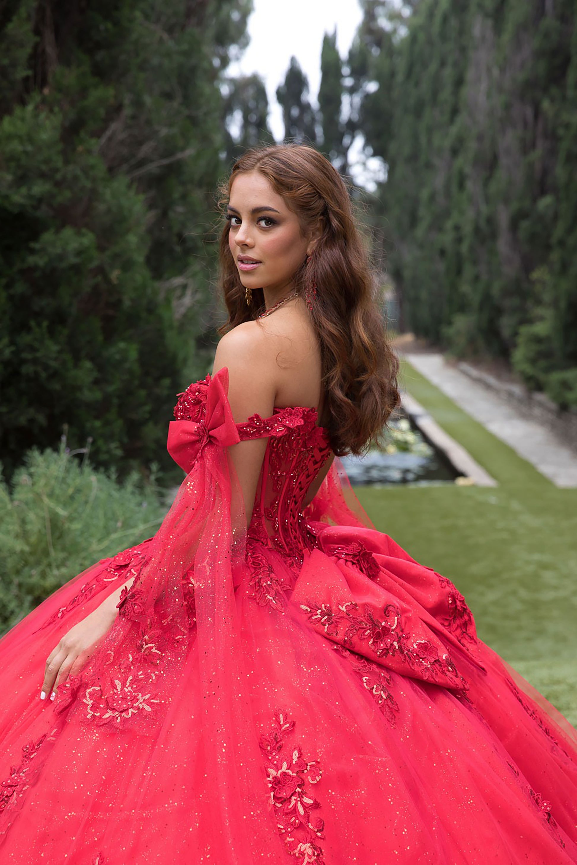 Woman in a red dress with floral details standing in a garden.