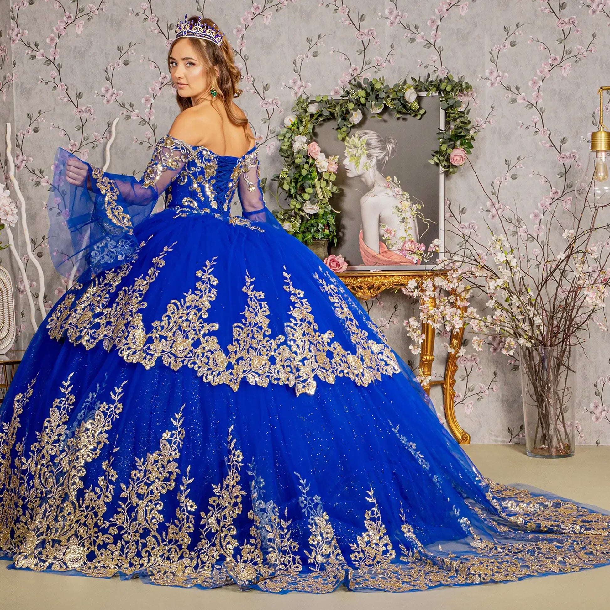 Woman in a blue and gold dress standing in a decorated room with floral arrangements.