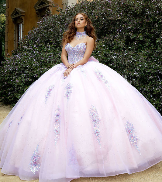 Woman in a pink and purple ball gown standing outdoors with greenery in the background