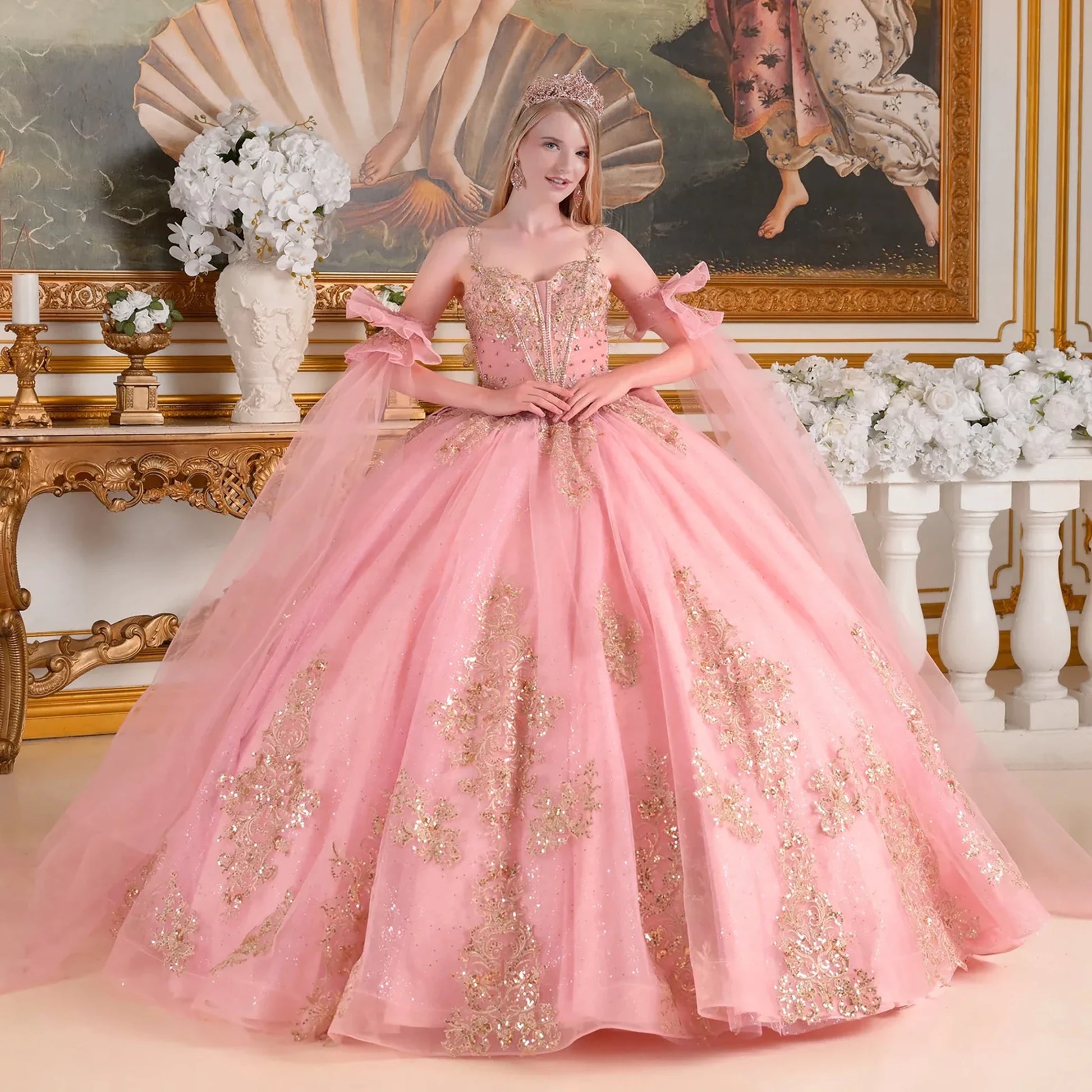 Woman in a dusty rose and gold gown standing in an ornate room with decorative elements.