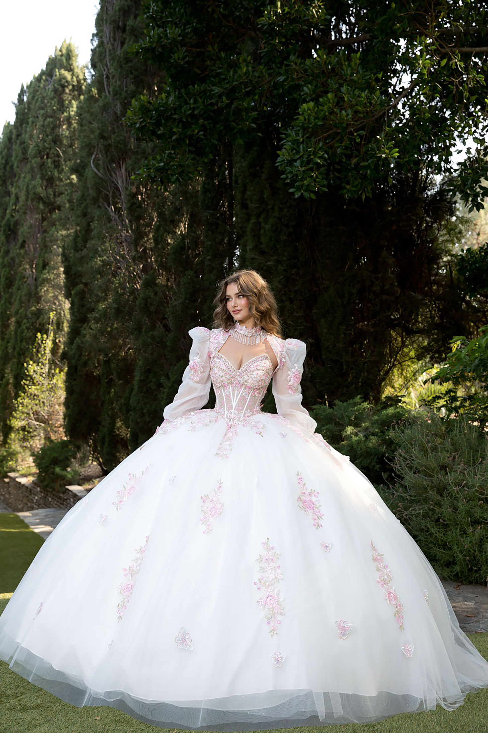 Woman in a white ballgown with floral embroidery standing outdoors.