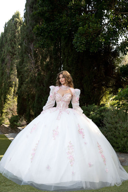 Woman in a white ballgown with floral embroidery standing outdoors.