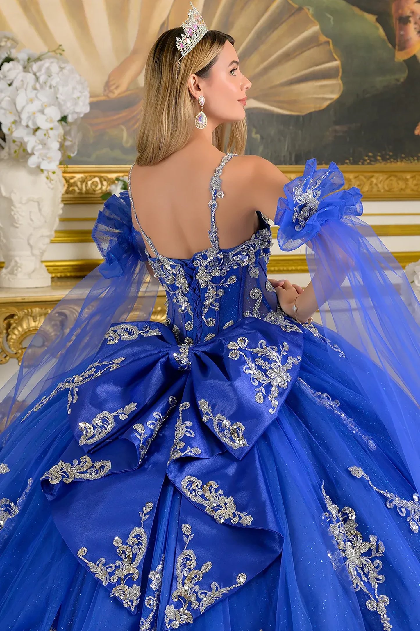 Woman in a blue formal gown with intricate designs, holding a matching bouquet, in an elegant indoor setting.