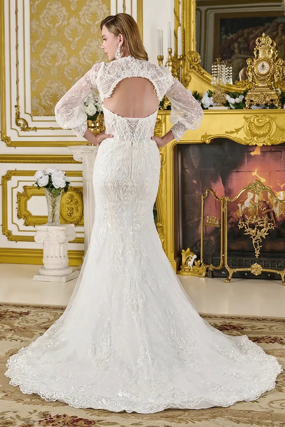 Woman wearing a white lace wedding dress in an ornate room with gold decorations.