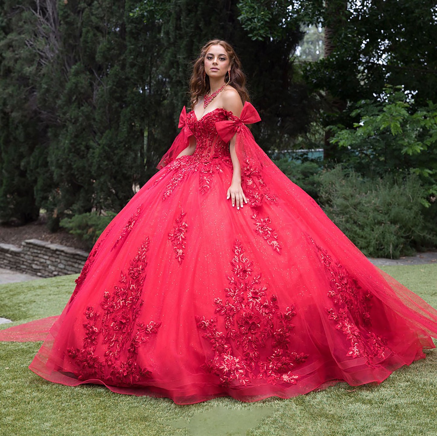 Woman in a red ball gown with floral details standing outdoors.