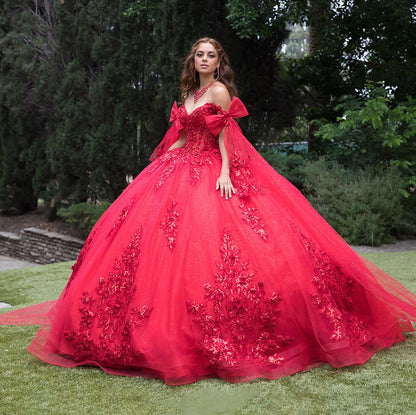 Woman in a red ball gown with floral details standing outdoors.