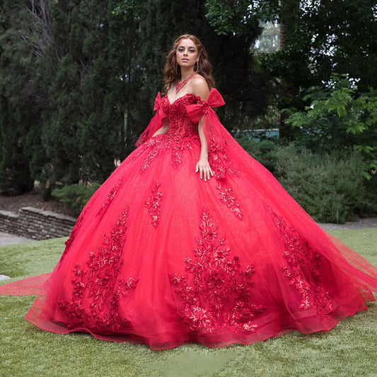 Woman in a red ball gown with floral details standing outdoors.