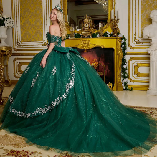 Woman in a green gown with floral details in an opulent room with gold accents.