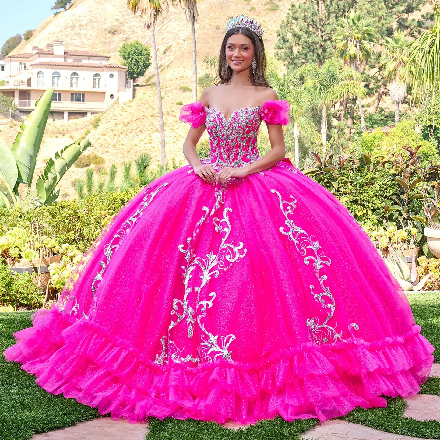 Woman in a fuchsia pink  quinceañera dress with white embroidery standing outdoors.